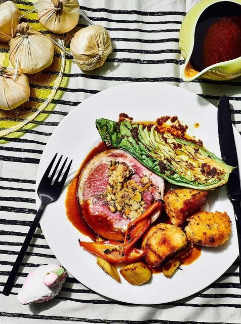 Overhead shot of a plated meat entree with cabbage, potatoes, and sauce, set on a striped tablecloth next to a gravy boat.
