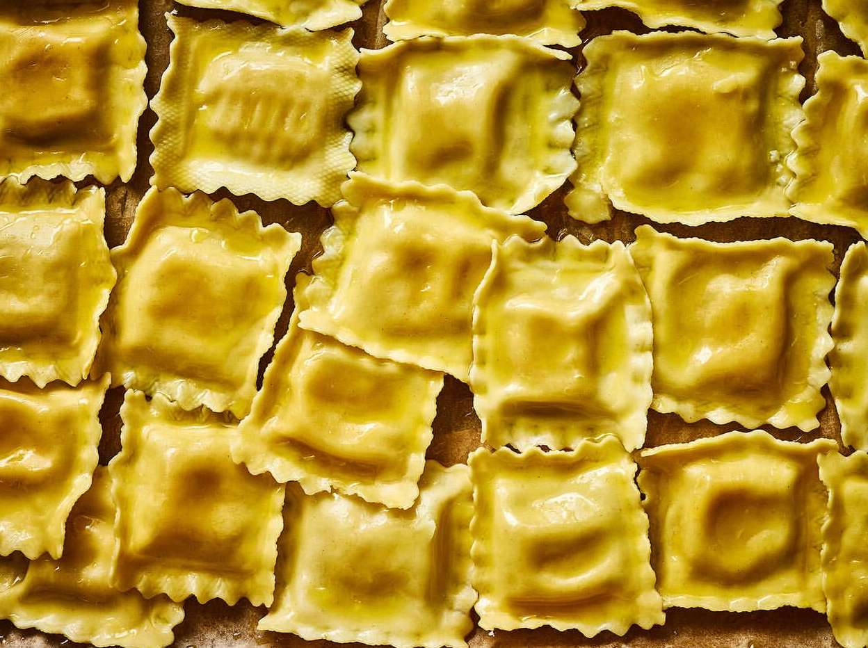 Close-up overhead shot of multiple square ravioli pasta with scalloped edges arranged on a flat surface, showcasing their shape and texture.