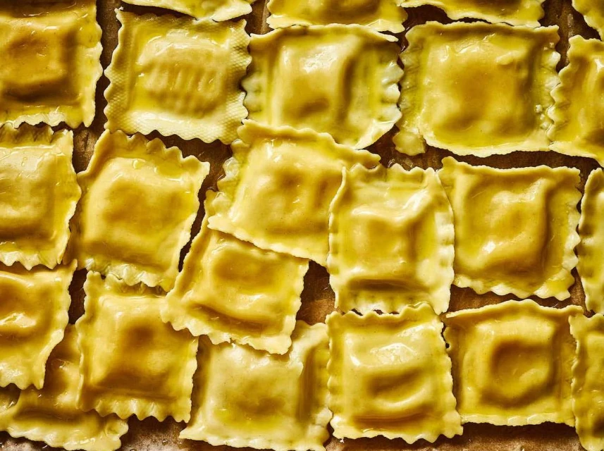 Close-up overhead shot of multiple square ravioli pasta with scalloped edges arranged on a flat surface, showcasing their shape and texture.