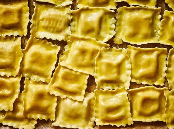 Close-up overhead shot of multiple square ravioli pasta with scalloped edges arranged on a flat surface, showcasing their shape and texture.