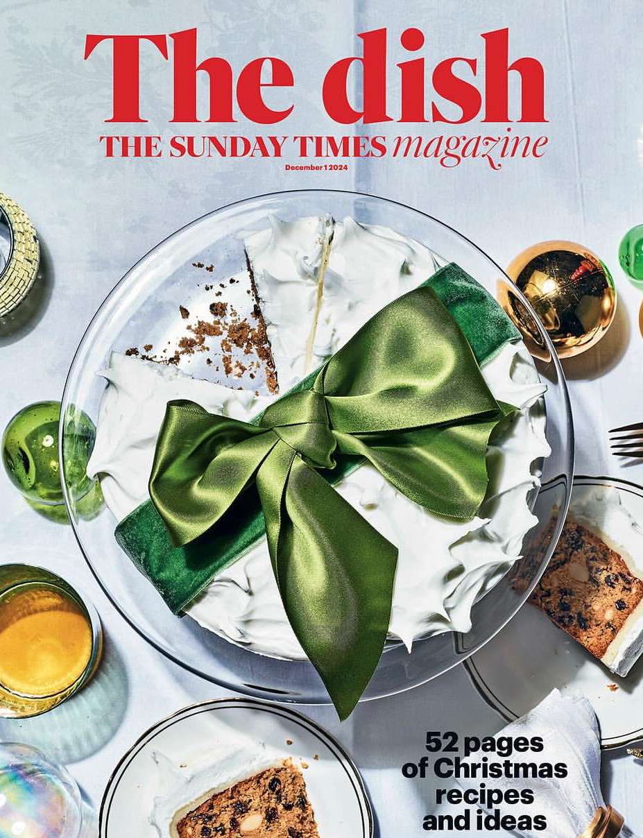Magazine cover featuring a cake with a green ribbon, Christmas ornaments, and a slice of cake, arranged on a white surface.