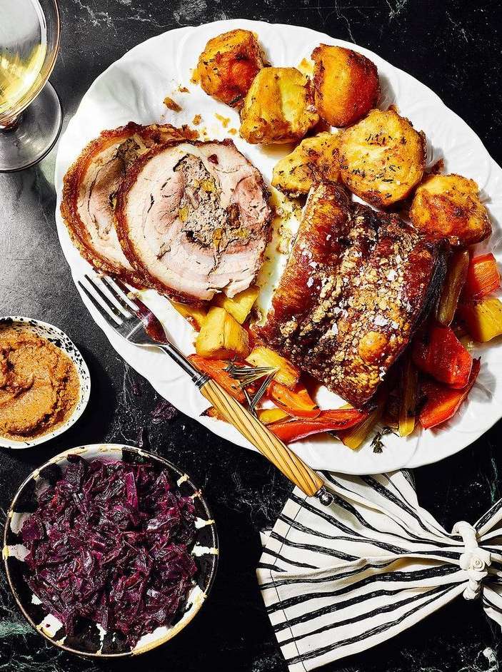 Overhead shot showcases a festive holiday dinner with roasted meats, potatoes, vegetables, and sauces on a dark marble surface.