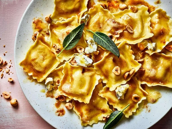 Overhead shot of ravioli with hazelnuts, sage, and cheese on a speckled ceramic plate, showcasing Italian cuisine and food photography.