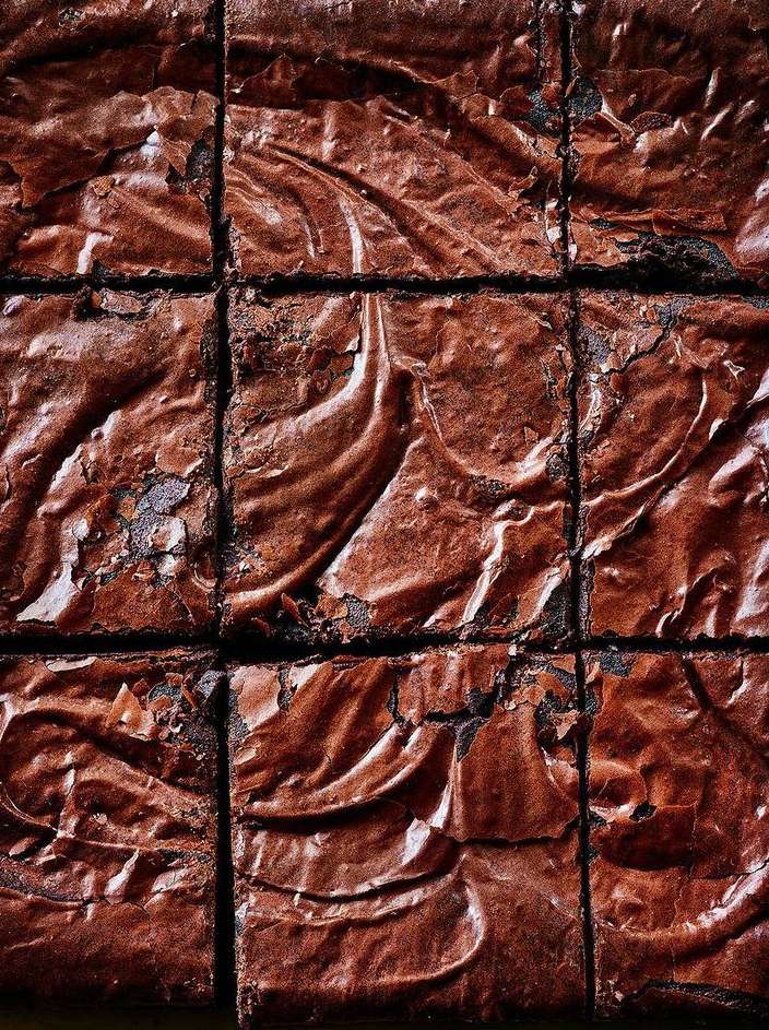 Overhead view of freshly baked chocolate brownies arranged in a grid pattern, showcasing their rich, swirled tops and dark color.