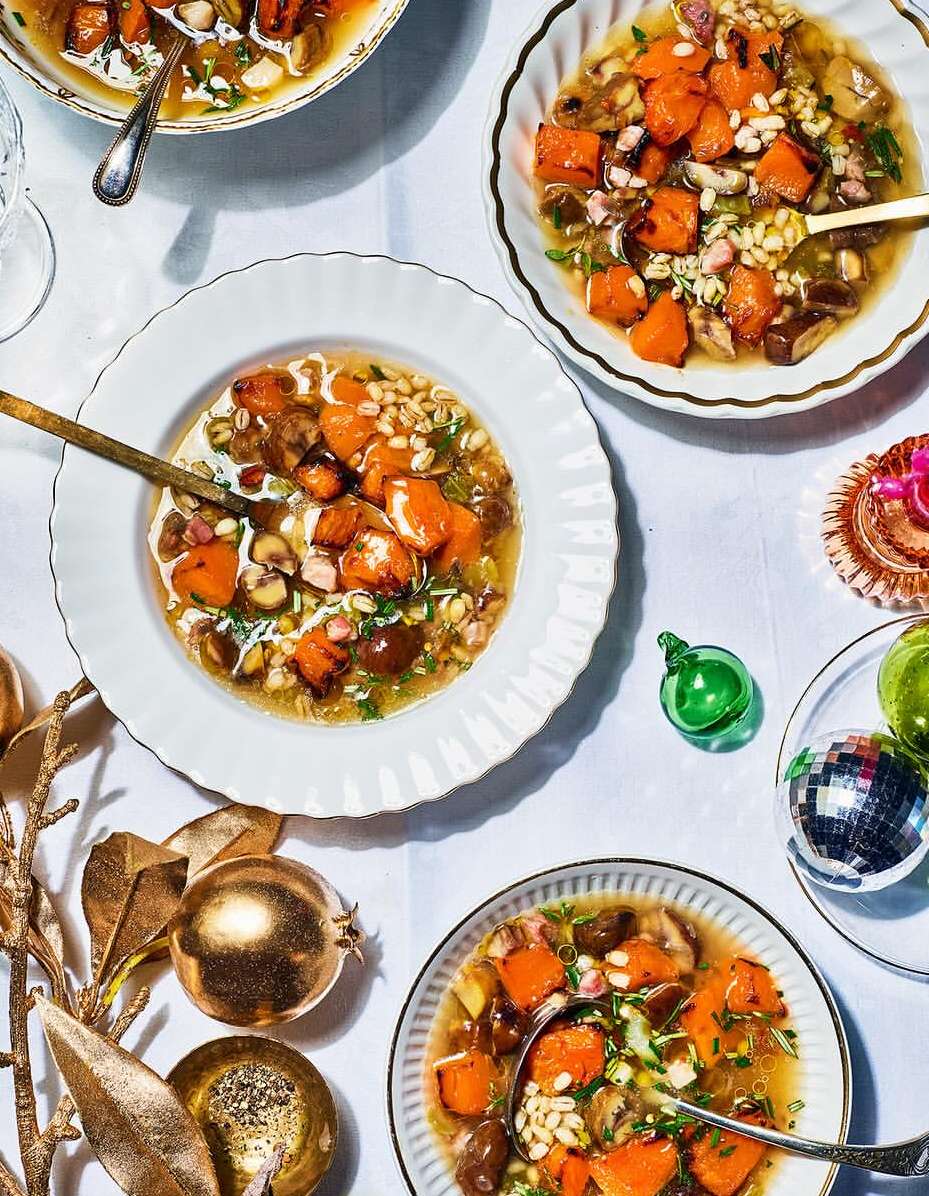 Overhead shot of four bowls filled with roasted butternut squash soup, decorated with golden ornaments on a white tablecloth.
