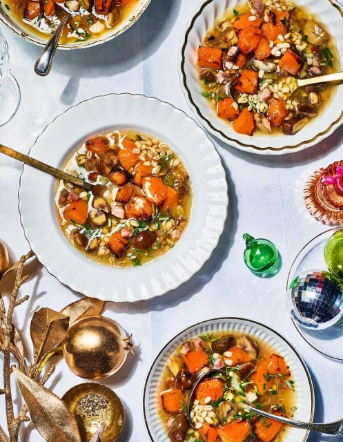 Overhead shot of four bowls filled with roasted butternut squash soup, decorated with golden ornaments on a white tablecloth.