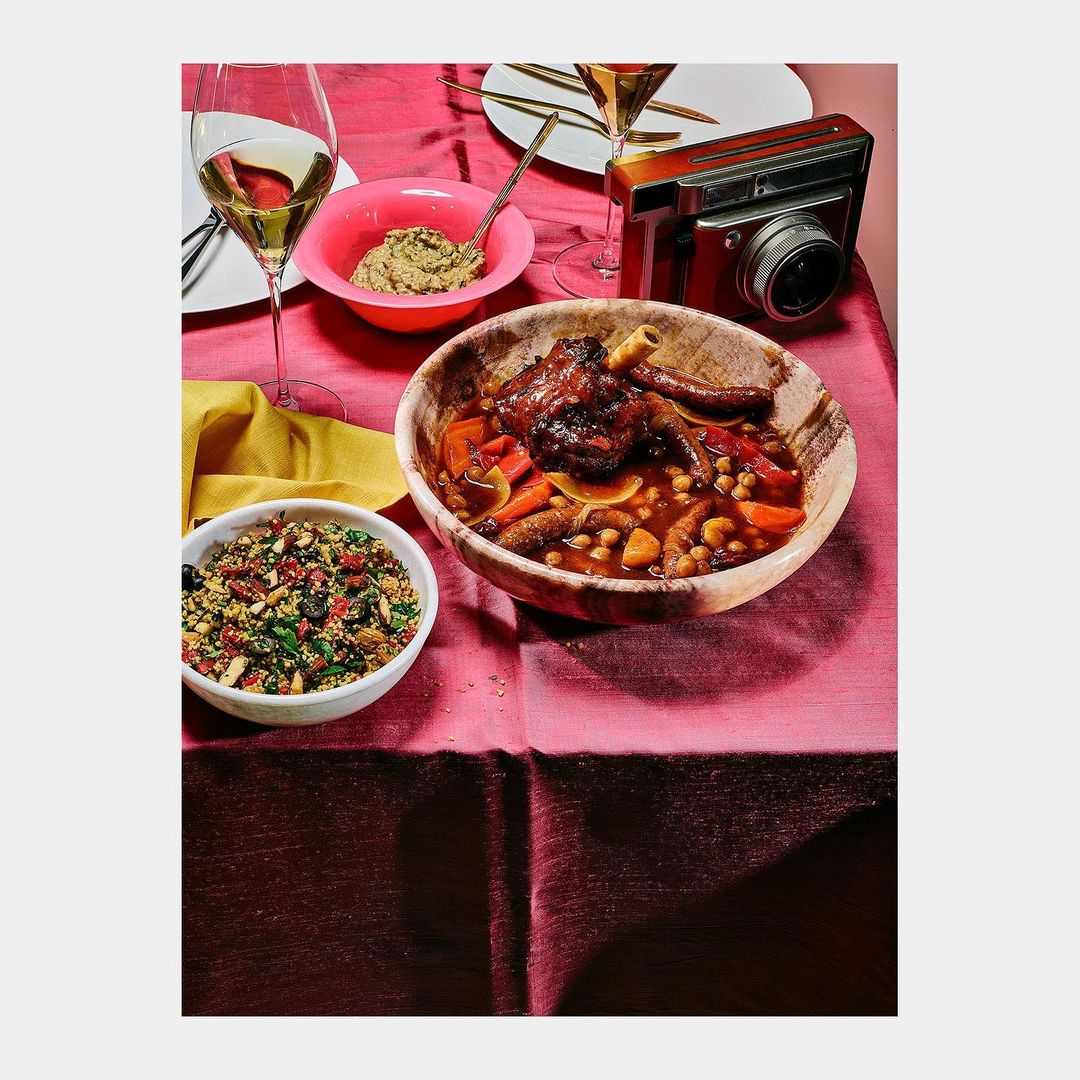Overhead shot of lamb shank tagine with carrots and chickpeas served in a wooden bowl, accompanied by quinoa and white wine.