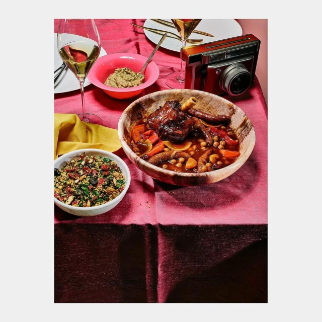 Overhead shot of lamb shank tagine with carrots and chickpeas served in a wooden bowl, accompanied by quinoa and white wine.