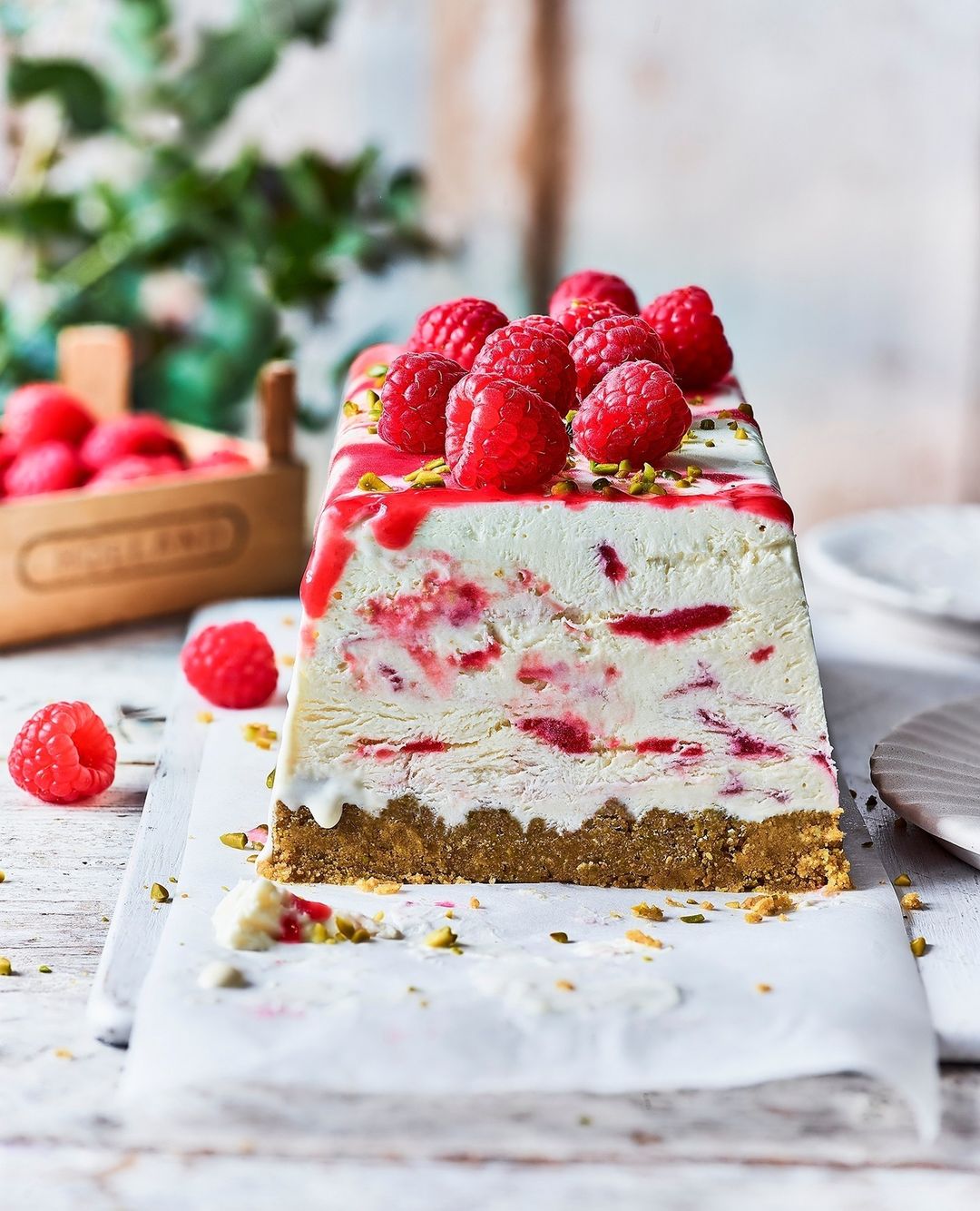 Overhead shot of a rectangular raspberry cake with a graham cracker base, a white creamy filling, and fresh raspberries on top.
