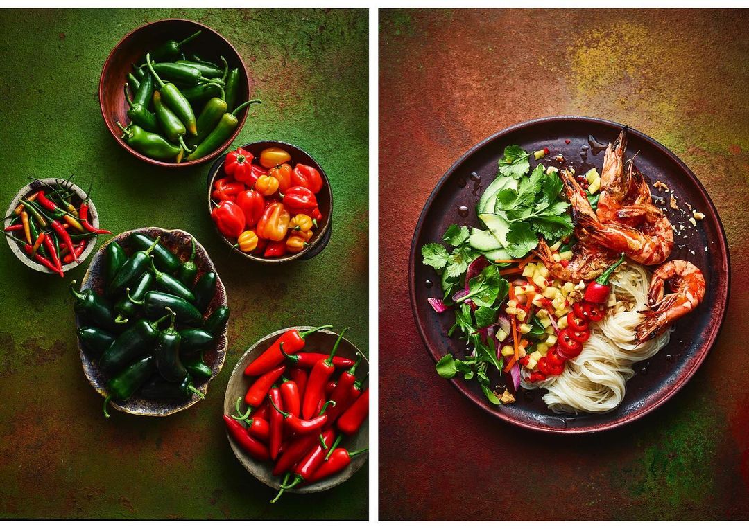 Overhead shot of colorful peppers, bowls of spices, and a plate of shrimp noodle salad; delicious and spicy food photography.