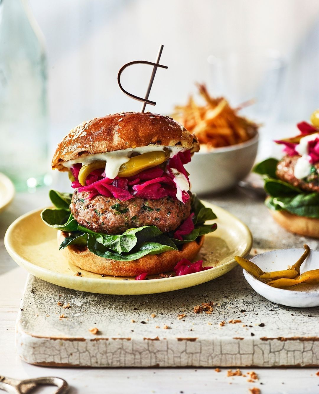 Close-up shot of a gourmet burger on a yellow plate with toppings like pickled red cabbage, lettuce, and white sauce on a wooden board.