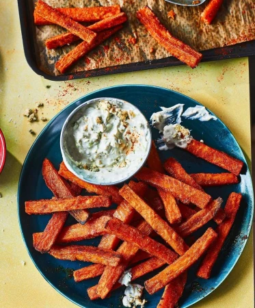 Overhead shot of sweet potato fries on a blue plate with dipping sauce, and more fries on a baking sheet, highlighting a food photography scene.
