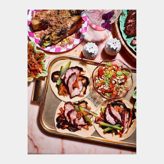 Overhead shot of a tray holding tacos and salads, including sliced meat, with plates, drinkware, and salt shakers in the background.
