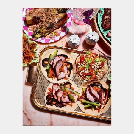 Overhead shot of a tray holding tacos and salads, including sliced meat, with plates, drinkware, and salt shakers in the background.