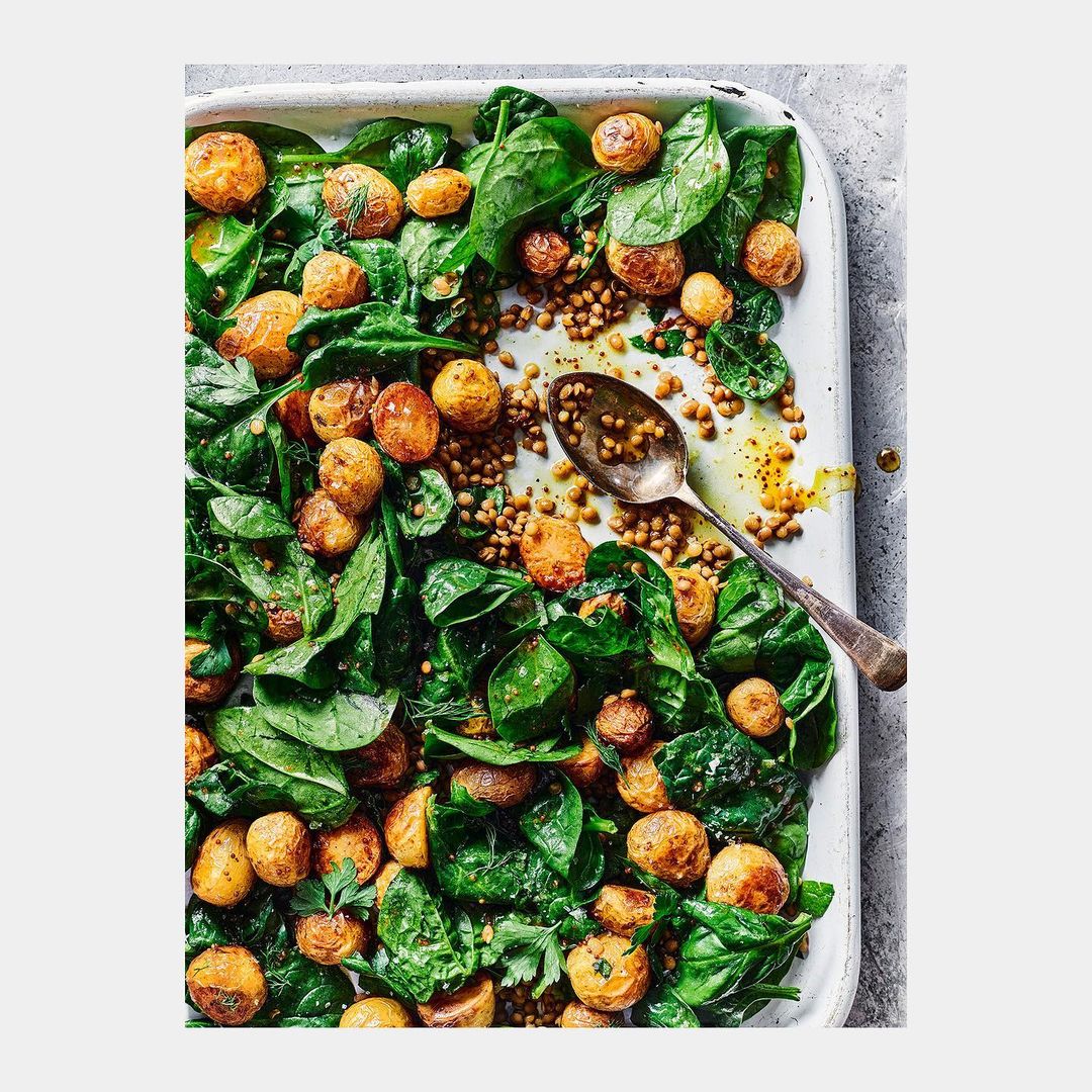 Overhead shot of a tray with spinach, lentils, and roasted potatoes, highlighted by a silver spoon, creating an inviting and healthy meal.