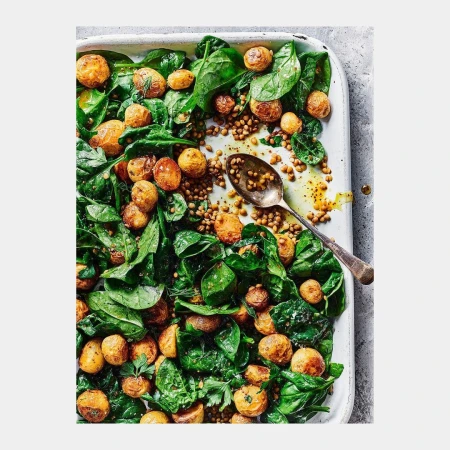 Overhead shot of a tray with spinach, lentils, and roasted potatoes, highlighted by a silver spoon, creating an inviting and healthy meal.