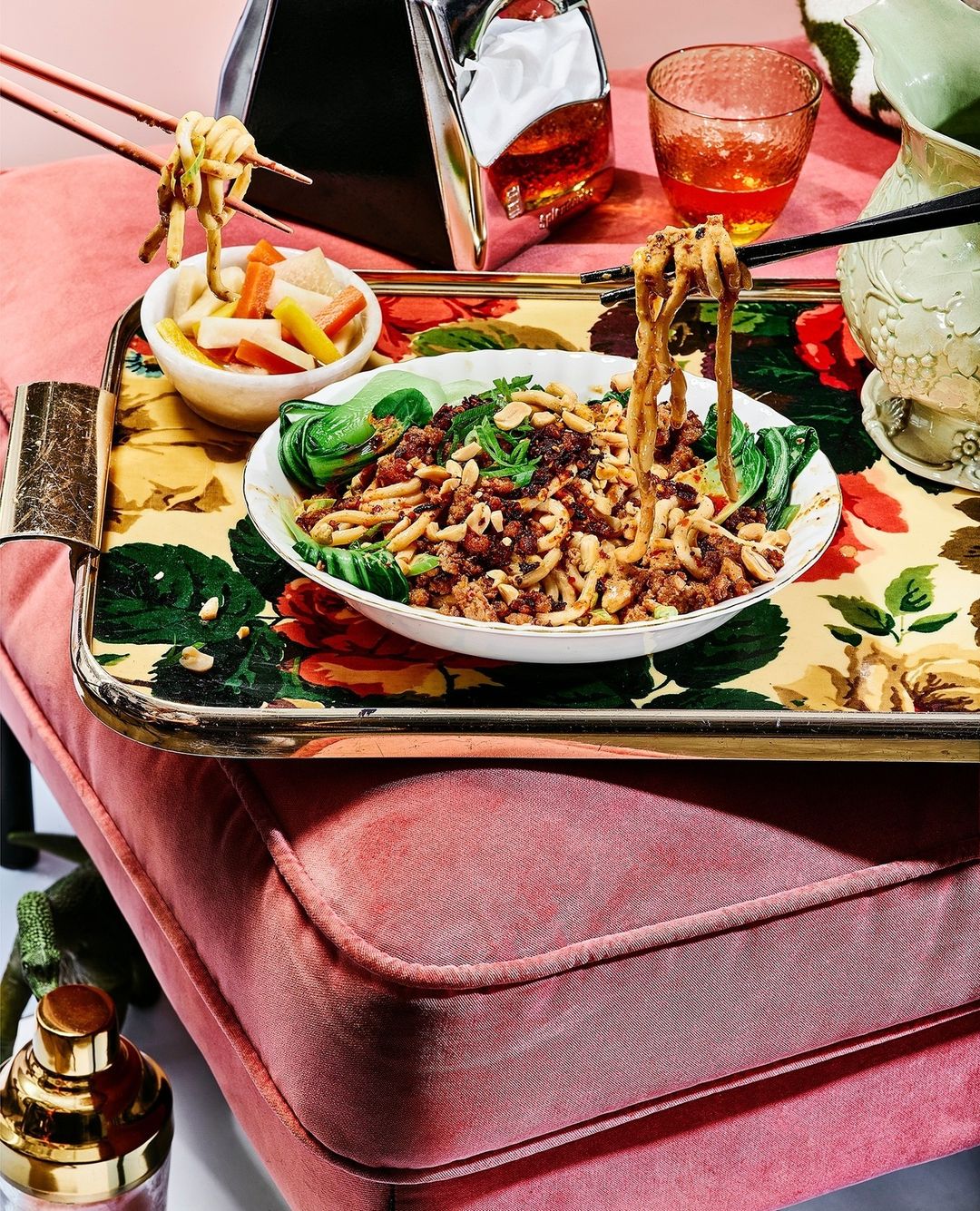 Overhead shot of a floral serving tray topped with a bowl of noodles, bok choy, and pickled vegetables, next to assorted glassware.