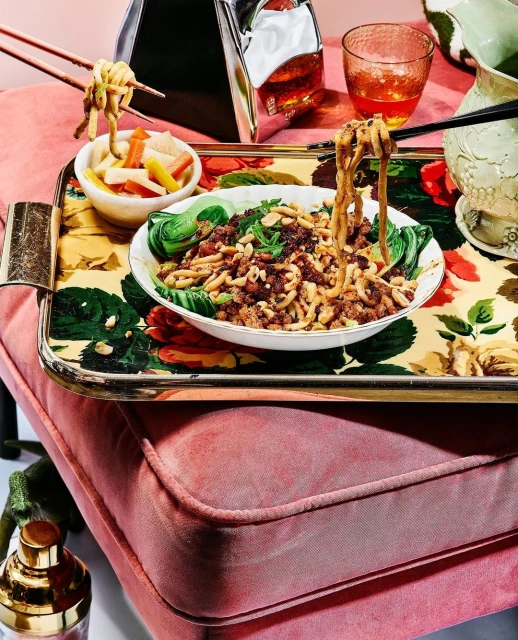 Overhead shot of a floral serving tray topped with a bowl of noodles, bok choy, and pickled vegetables, next to assorted glassware.