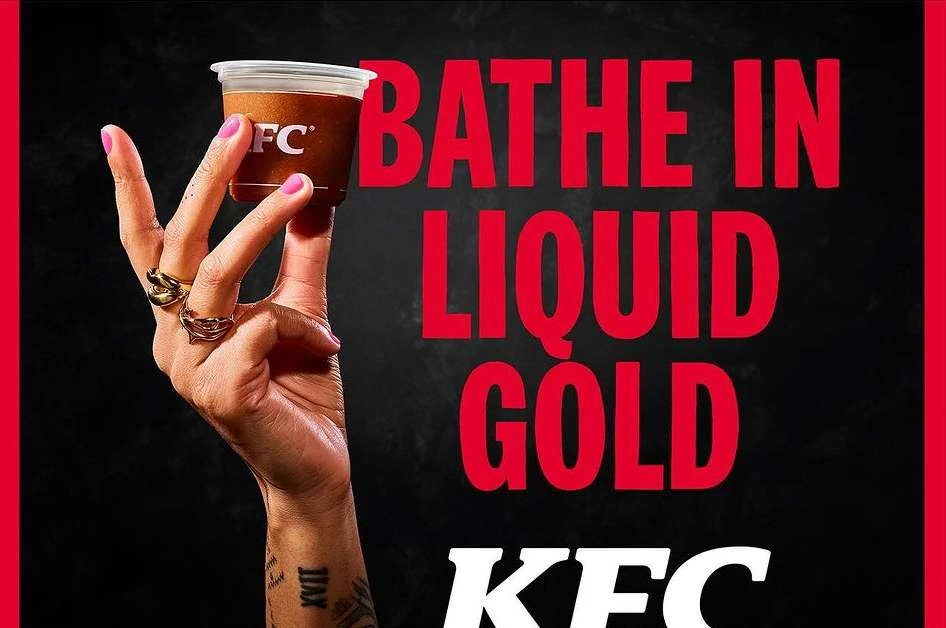 Close-up of adult hand holding KFC gravy cup, studio lighting, vibrant colors, food and beverage promotion, black background.
