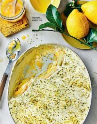 Overhead food photography of limoncello and pistachio tiramisu in a ceramic dish with fresh lemons and a glass jar of curd.