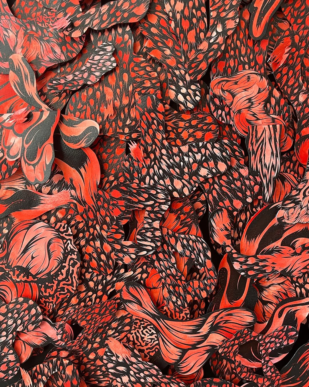 Abstract paper art collage featuring densely layered, swirling shapes in vibrant shades of red and black, creating a textured, patterned surface.