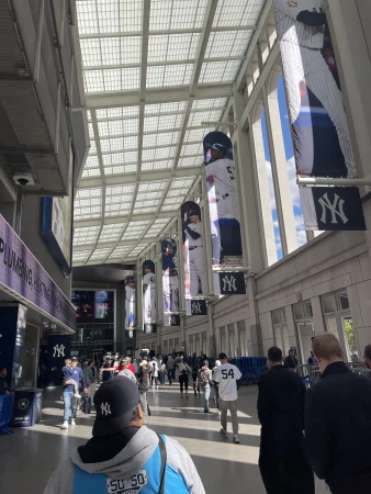 Crowd walking through a stadium concourse with large vertical baseball player banners hanging from a high glass roof.