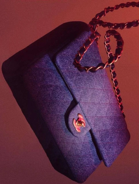 Denim Chanel handbag with gold chain strap on a gradient red and purple backdrop.  High-fashion luxury accessory with signature logo detail.