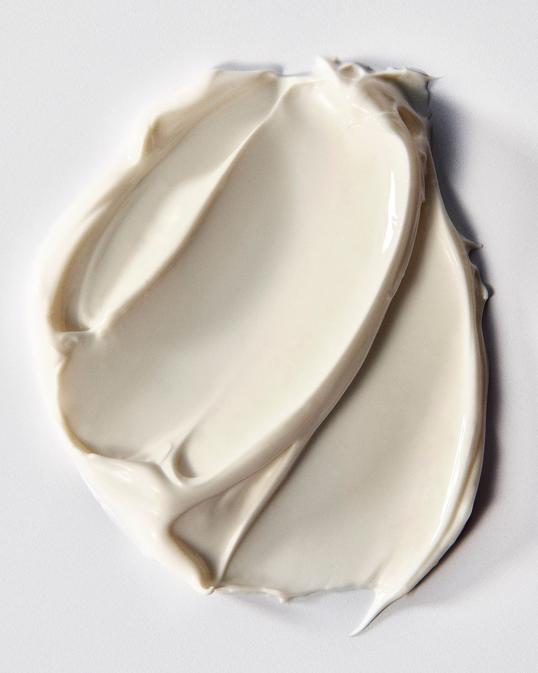 Close-up of a thick, light beige cream swatch with smooth, swirling textures on a white surface. Beauty product shot.