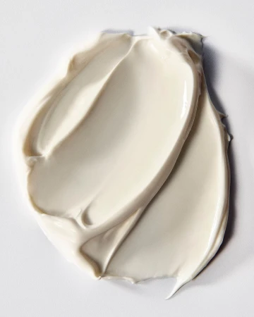 Close-up of a thick, light beige cream swatch with smooth, swirling textures on a white surface. Beauty product shot. 