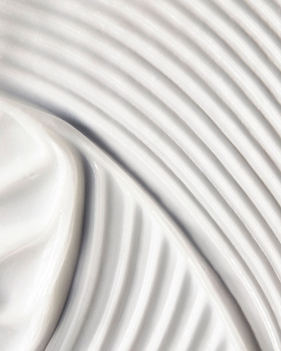 Close-up shot of thick, white cream with curved patterns. The texture is smooth, and the color palette is neutral and clean.