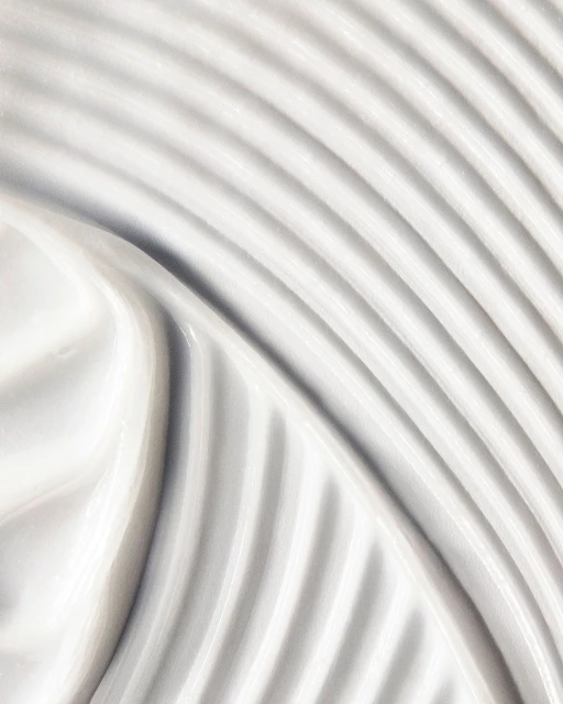 Close-up shot of thick, white cream with curved patterns. The texture is smooth, and the color palette is neutral and clean.