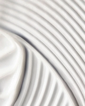 Close-up shot of thick, white cream with curved patterns. The texture is smooth, and the color palette is neutral and clean.