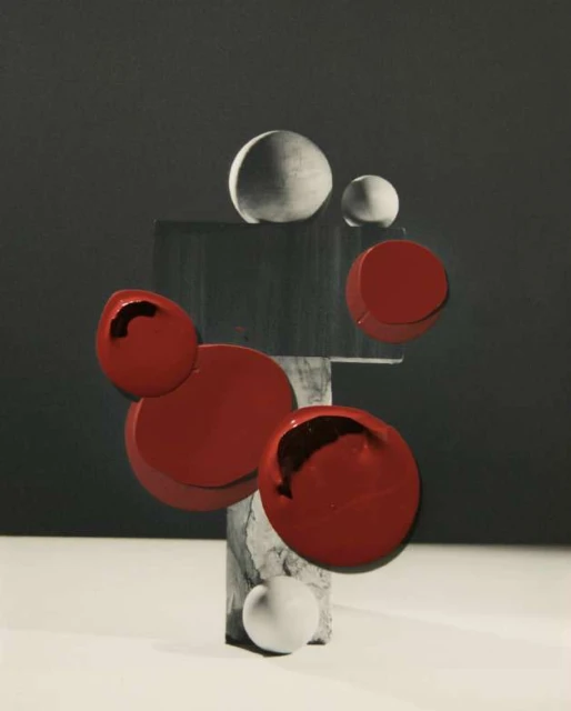 Abstract still life photography features red and white spheres, and geometric shapes on a grey surface and background.