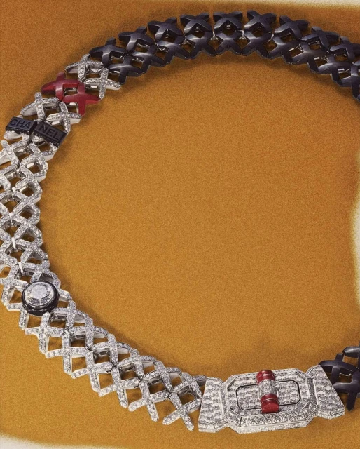 Close-up of a designer chain necklace in silver, black, and red on a mustard-yellow background, featuring the Chanel logo.