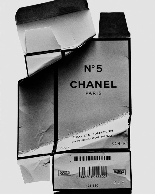 Close-up of a damaged Chanel No. 5 perfume box in black and white. The focus is on the iconic branding and product information.