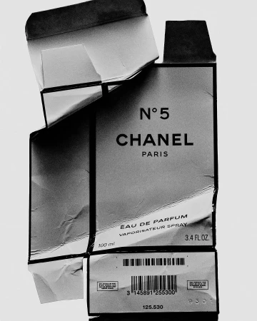Close-up of a damaged Chanel No. 5 perfume box in black and white. The focus is on the iconic branding and product information.