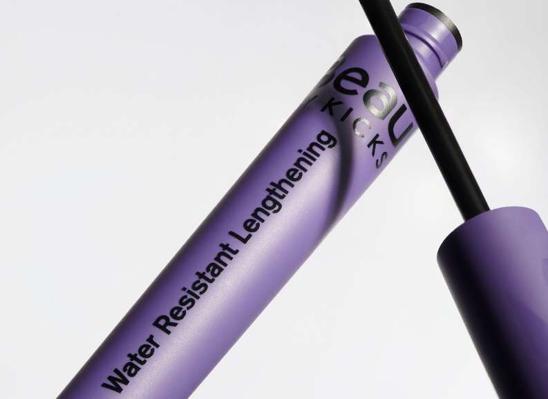 A close-up studio shot of a purple tube of BEAU KICKS water-resistant lengthening mascara with a black applicator wand.