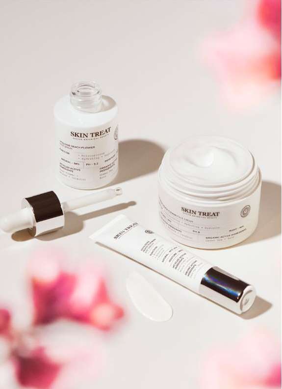 Cosmetic product arrangement featuring a serum bottle with dropper, a cream jar, and a tube of lotion on a bright surface.