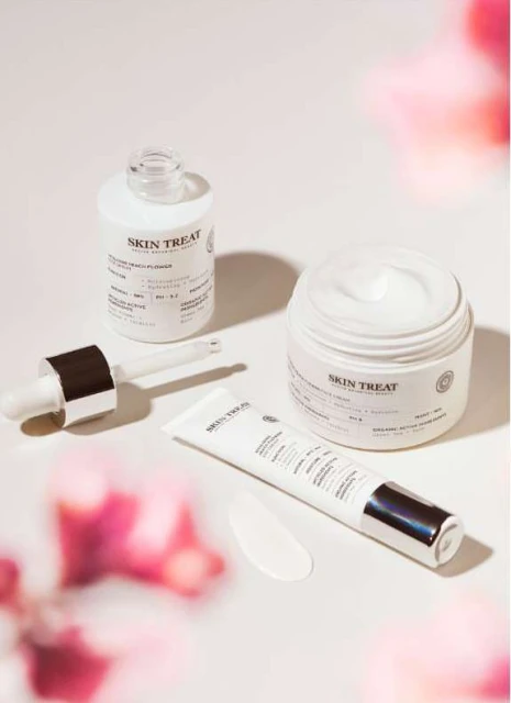 Cosmetic product arrangement featuring a serum bottle with dropper, a cream jar, and a tube of lotion on a bright surface.