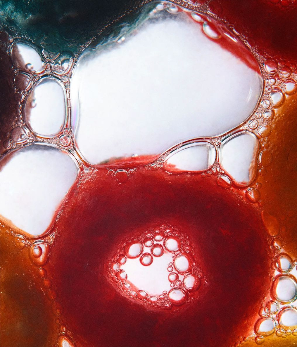Macro photograph of vibrant, colorful liquid and soap bubbles forming an abstract design with shades of red, orange, green and white.