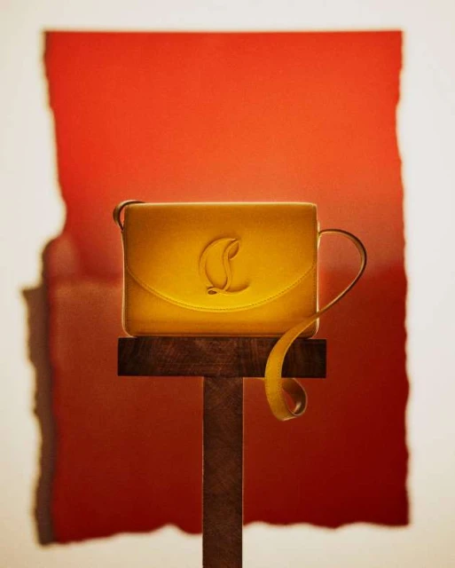 Yellow leather purse on a brown wooden pedestal against an abstract red and white background, product shot, luxury fashion accessory.