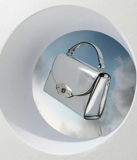 Silver leather satchel handbag featured in a circular cutout against a blue and white abstract background in a product studio shot.