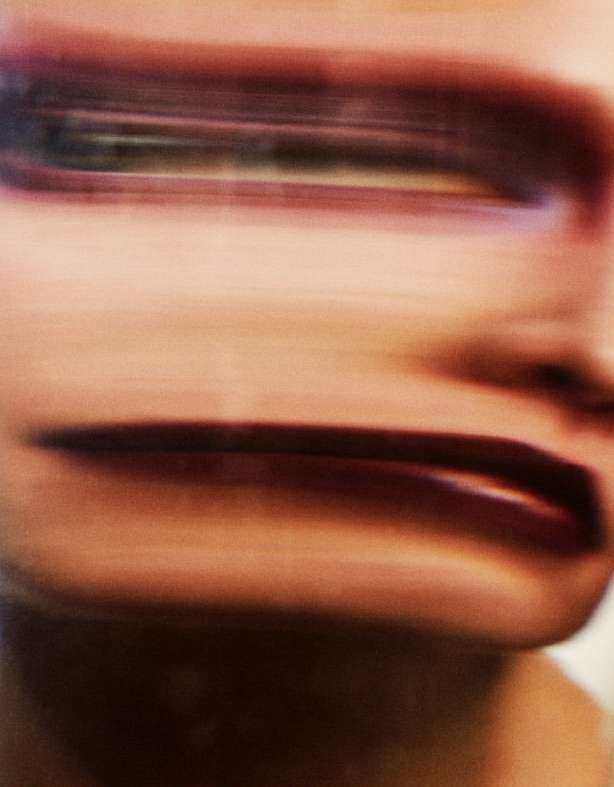 Close-up, blurred view of an adult human face featuring bold red lipstick, dark eye makeup, and soft, blurred skin texture.