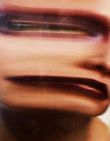 Close-up, blurred view of an adult human face featuring bold red lipstick, dark eye makeup, and soft, blurred skin texture.