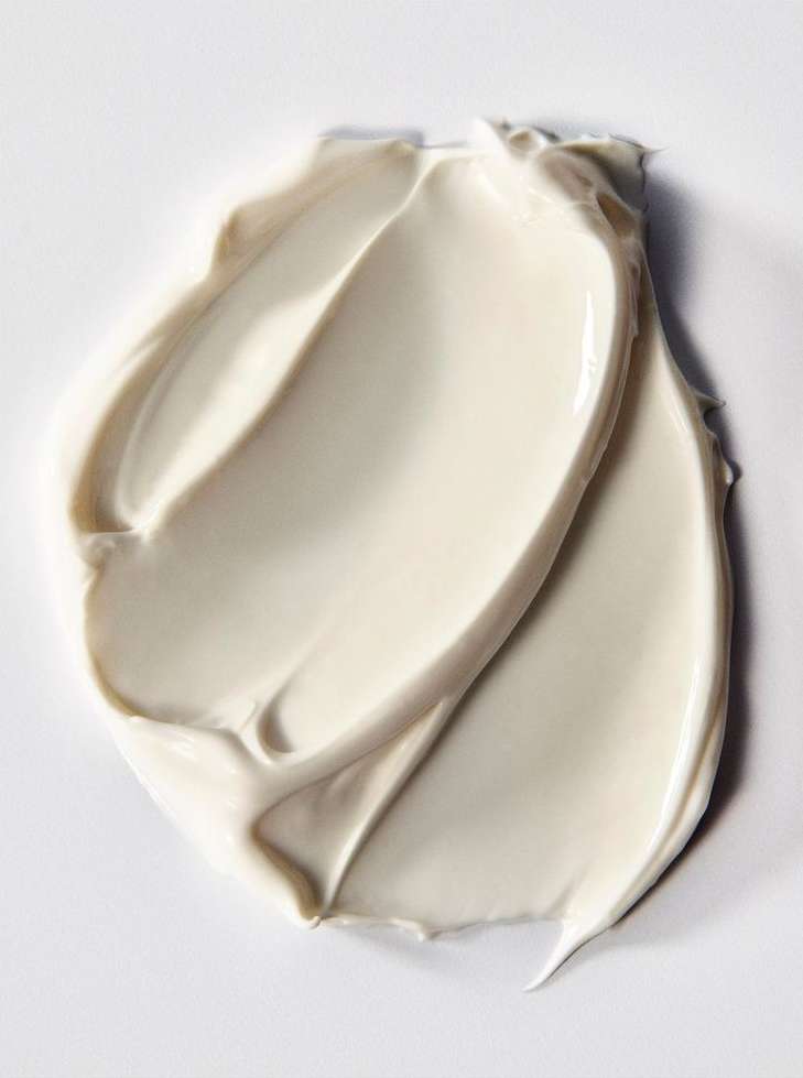 Close-up shot of thick, swirled, creamy white beauty product. The texture is smooth and glossy, set against a neutral background.