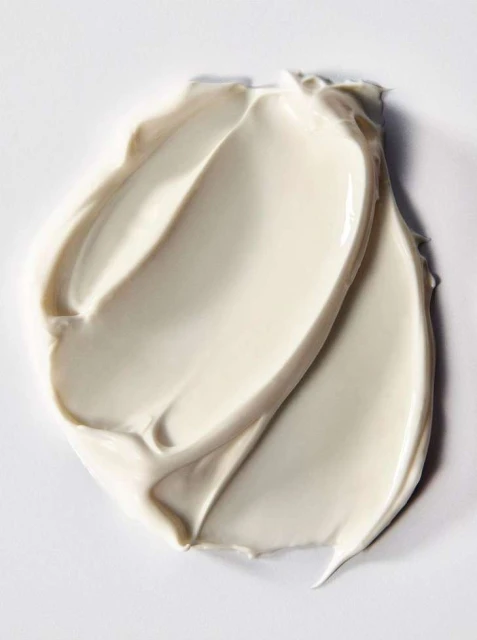 Close-up shot of thick, swirled, creamy white beauty product. The texture is smooth and glossy, set against a neutral background.