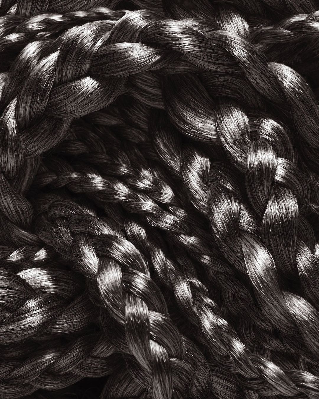Braided textile close-up displaying interwoven strands in a pattern, highlighting textures and dimensional forms with light and shadow.