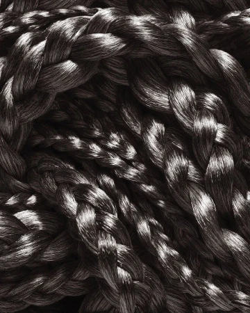 Braided textile close-up displaying interwoven strands in a pattern, highlighting textures and dimensional forms with light and shadow.