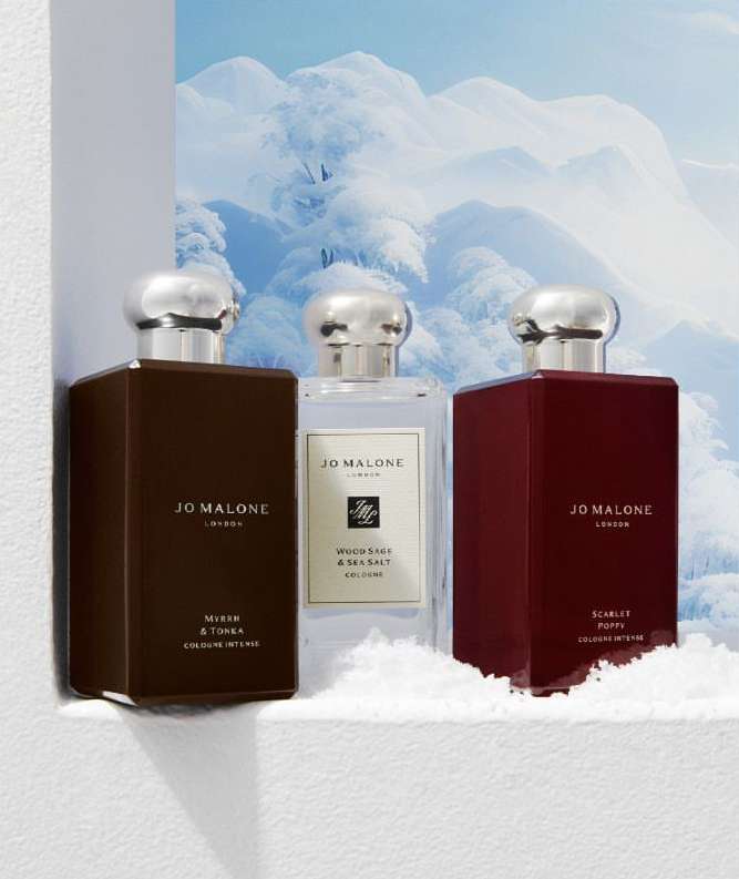 Three Jo Malone London cologne bottles in different colors displayed against a snowy mountain backdrop in a fragrance product shot.