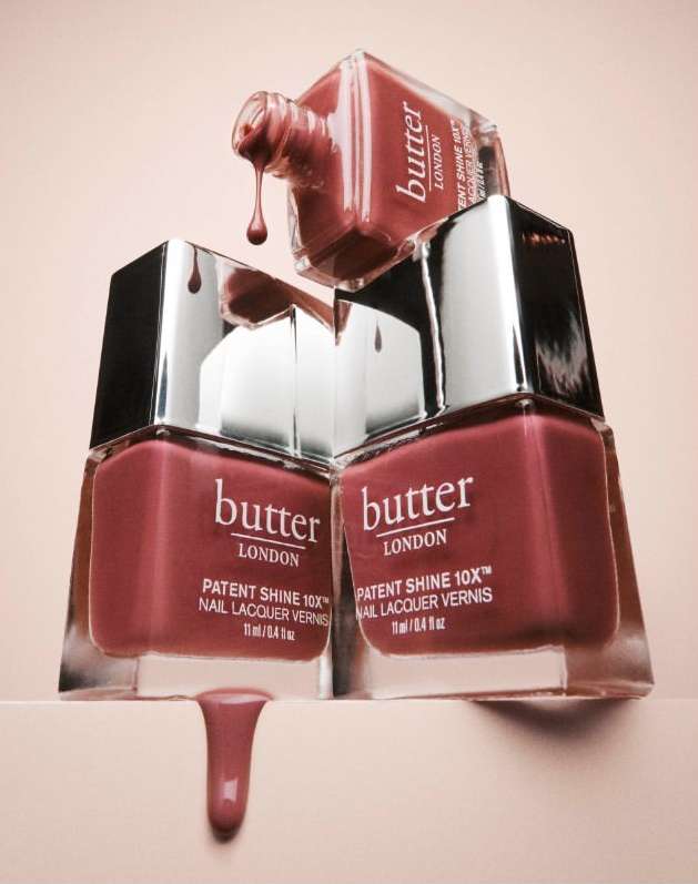 Close-up studio shot of Butter London nail polish bottles stacked with drips of nail lacquer, emphasizing color and shine for beauty advertising.